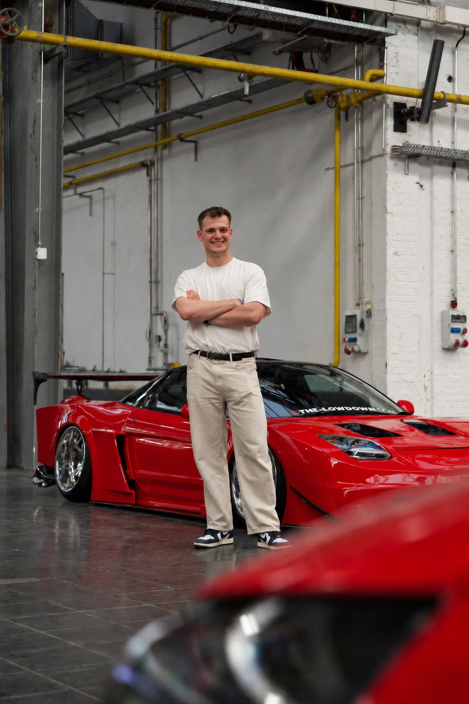 Tobias Rudolph vor einem roten Sportwagen in einer Industriehalle